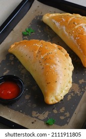 Folded Pizza Or Calzone Is A Dish From Italy, Made From Salted Bread And Stuffed With Pizza Topping And Cheese. Baked In Oven And Placed In Black Pan. Take By Selective Object. Defocused Or Blurred