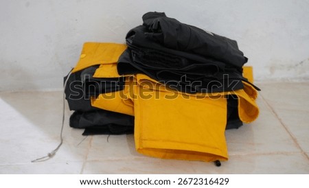 Folded Raincoats Stack, A stack of folded raincoats in yellow and black colors placed on the floor. Waterproof clothing for rainy season and outdoor protection.