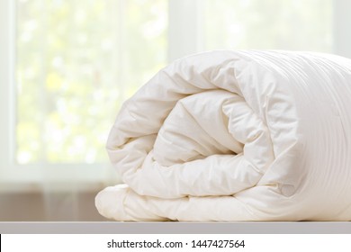 A folded rolls duvet is lying on the dresser against the background of a blurred window. Household.