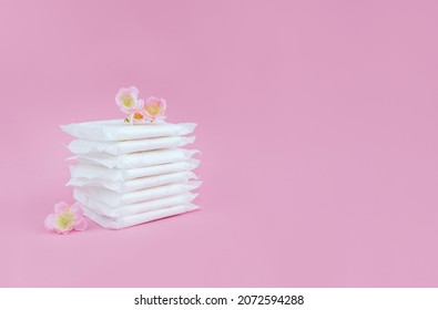Folded sanitary pads and flowers on pink background. Menstrual cycle concept. Copy space