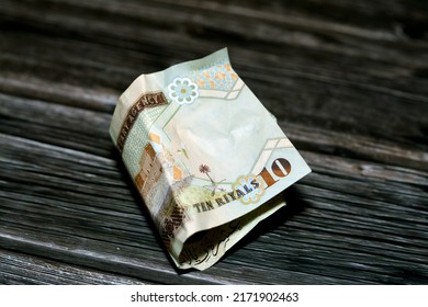  Folded Saudi Arabia money of 10 SAR ten riyals isolated on wooden background, Crumpled 10 Saudi Riyals cash bill banknote, Saudi money inflation and economy world crisis concept, selective focus