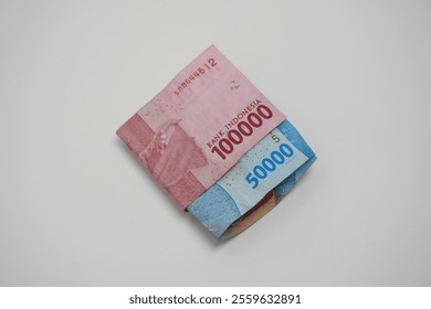 Folded two sheets of Rupiah banknotes (Indonesian currency) with the following denominations: fifty thousand rupiah (blue), and one hundred thousand rupiah (red).