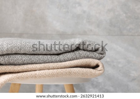 Folded woolen plaids on table near grey wall, closeup
