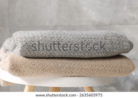 Folded woolen plaids on table near grey wall, closeup