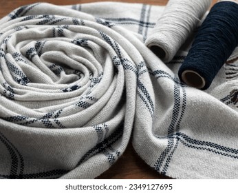 Folded woolen white and dark blue scarf or shawl or plaid and bobbins with yarn, selective focus. Hand woven project