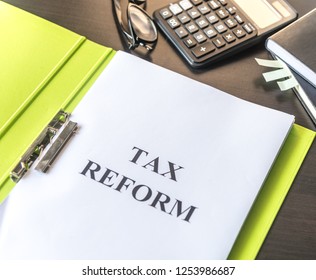Folder and documents about Tax Reform with calculator and glasses on table background.