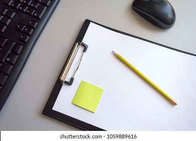 A folder for papers with a white sheet, a green sticker and a yellow pencil on a gray background with a black computer mouse and keyboard - Powered by Shutterstock