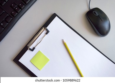 A folder for papers with a white sheet, a green sticker and a yellow pencil on a gray background with a black computer mouse and keyboard - Powered by Shutterstock