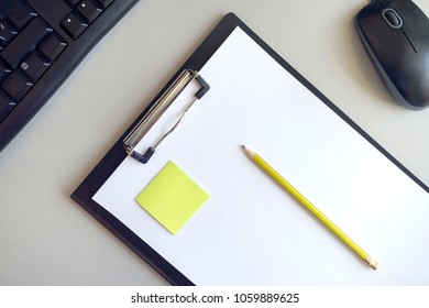 A folder for papers with a white sheet, a green sticker and a yellow pencil on a gray background with a black computer mouse and keyboard - Powered by Shutterstock