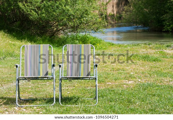 Folding\
camping chairs on the green lawn by the\
river