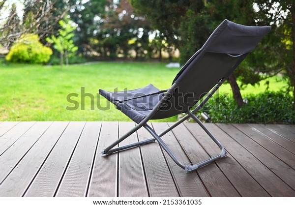 Folding chair surrounded by green\
leaves on a wooden deck. Relaxation in the garden. Cottage\
aesthetics. Vacation outside the city. Warm summer day.\
terrace