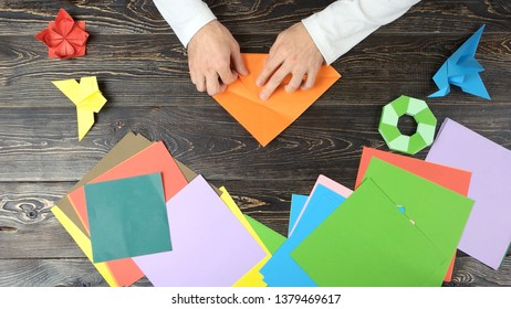 Folding Origami Paper In Triangle, Top View. Man Making Origami Figures. Colourful Papers.