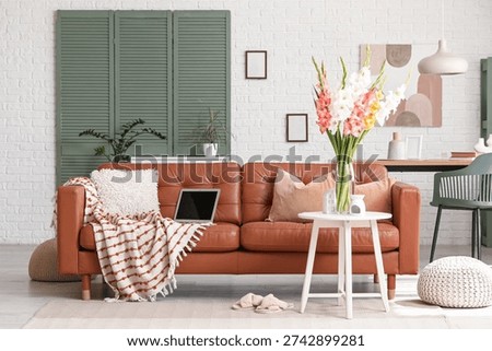 Folding screen, comfortable sofa, table and vase with gladiolus flowers in interior of living room
