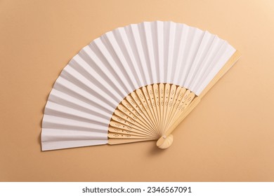 Folding traditional white hand fan for summer mock-up. Beige background
