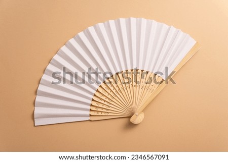 Folding traditional white hand fan for summer mock-up. Beige background
