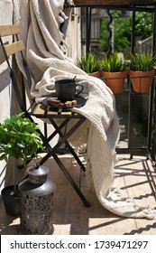 Folding Wood Chair With Knitted Blanket And Coffee Mug, Plants And Lantern At Sunny Day. Small Apartment Balcony Decor.