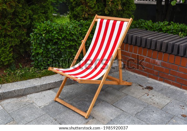 folding wooden\
chair hammock with red striped fabric on the street. chair chaise\
longue, summer vacation,\
backyard