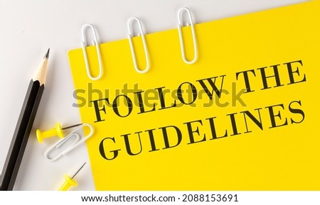FOLLOW THE GUIDELINES word on yellow paper with office tools on white background