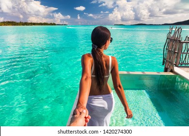 Follow Me Beach Couple Man Holding Girlfriend Hand Following Woman To The Swimming Pool Blue Ocean Vacation In Bora Bora, Tahiti ,French Polynesia.
