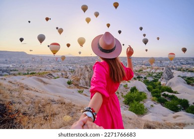 Follow me concept. Traveling couple walking together in valley in Anatolia, Kapadokya. Flying air balloons at beautiful destination in Nevsehir, Goreme
