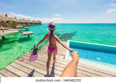 Follow Me Luxury Travel Vacation Couple Following Woman Snorkeling At Overwater Bungalow Hotel. Man Holding Hand Following Woman In Bora Bora, Tahiti, French Polynesia. Watersport Fun Activity.
