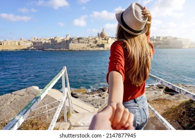 Follow Me In Malta. Young Carefree Tourist Woman In Hat Holds Boyfriend Hand And Looking Panoramic View Of Valletta, Malta. Couple On Summer Holiday Vacation. Traveling Together.	