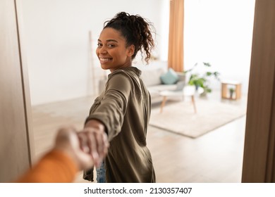 Follow Me To My Home. Happy African American Lady Opening Door Holding Hand Leading To Her Living Room, Smiling To Camera Indoors. Real Estate Ownership Concept. Selective Focus