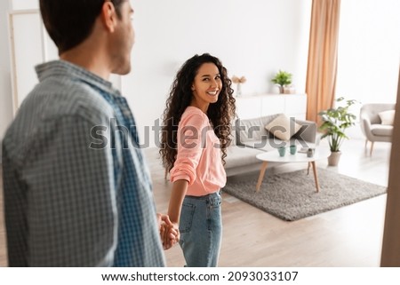 Follow Me. Portrait of happy lady inviting guy to enter home, welcoming to living room, happy smiling woman holding man's hand showing new modern apartment and living room, selective focus