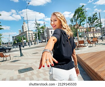 Follow me - POV. A beautiful tourist girl walks around the city and invites you to follow her. The girl turns over her shoulder and stretches her hand back. The concept of friendship and trust.