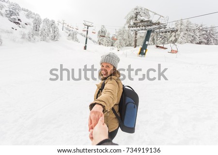 Follow me in ski resort. Young woman holding man by hand going to winter nature in mountains.