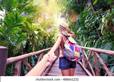 Follow Me. Travel Concept. Back View Of Young Woman With Backpack Outdoors Discovering Jungle Holding Boyfriend's Hand.