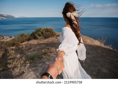 Follow me. A young girl in a white dress leads a man by the hand to the cliff. Look at her blue sea. The dress and hair are fluttering in the wind. The concept of freedom