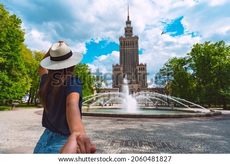 Follow me. Young tourist woman in white sun hat holding her boyfriend by hand and walking in Warsaw city. Couple on summer holiday vacation in Poland. Traveling together.