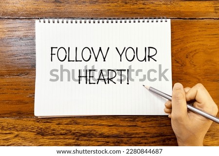 Follow your heart handwriting text on blank notebook paper on wooden table with hand holding pencil. Business concept about following your dream.