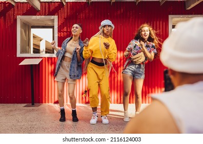 Following fun social media trends. Group of generation z friends doing trendy dance moves in front of a camera phone. Vibrant young people creating content for their social media vlog.