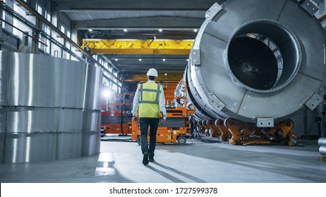 Following Shot Of Heavy Industry Engineers Walking Through Manufacturing Factory. In The Background Professionals Working On Construction Of Oil, Gas And Fuel Pipeline Transportation Products