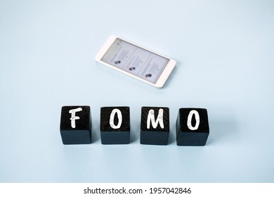 FOMO, Fear of missing out, social anxiety, stay continually connected, fear of regret, Social networking. FOMO text with blurred cell phone with social Media icons on blue background