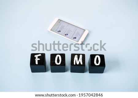 FOMO, Fear of missing out, social anxiety, stay continually connected, fear of regret, Social networking. FOMO text with blurred cell phone with social Media icons on blue background