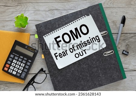FOMO. text in notepad in a folder. near a yellow notepad with a calculator