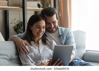 Fond memories. Smiling spouses hug on sofa recall sweet moments of life to mind watch wedding video on electronic pad. Young couple in love browse online travel agencies websites plan honeymoon trip