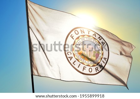 Fontana of California of United States flag waving on the wind in front of sun