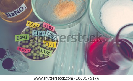 Food additives: chemical additives in the form of granules with colored labels, sodium nitrate in a flask, sugar and glutamate on a laboratory bench. Top view.