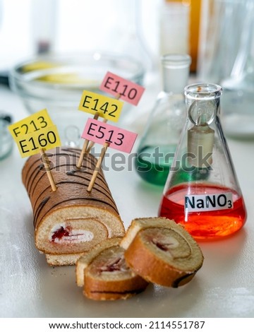 Food additives: sweet roll with chemical additives with colored labels, on a laboratory table. Close up.