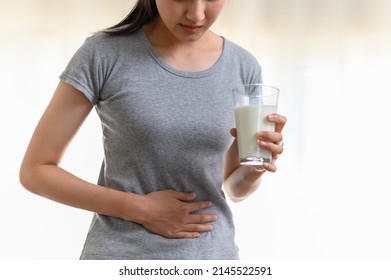 Food allergy milk lactose allergen health care illness concept. Close up hand of young Asian woman holding stomach belly feel pain unhappy after drink a glass of milk.