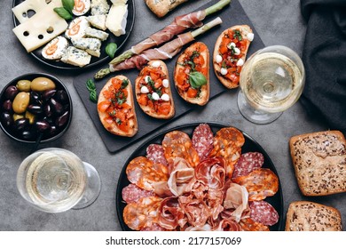 Food antipasto prosciutto ham, salami, olives and  bread sticks. cheese on a board parmesan, pecorino, gorgonzola. Tomato and basil bruschetta. Two glasses of white wine or Prosecco