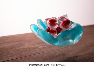 Food Art. An Ice Sculpture In The Shape Of A Hand Holds Frozen Raspberries In Ice Cubes. Copy Space