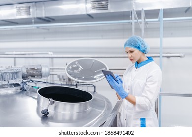 Food Automated Modern Industrial Production. Operator Worker Woman Checks Steel Tanks With Milk With Tablet Computer.