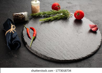 Food background with empty stone plate,fresh rosemary,garlic,tomato,chili pepper and pink sea salt on black table. - Powered by Shutterstock