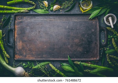 Food background with free space for text. Herbs, olive oil, spices around cast iron frying board. Top view.