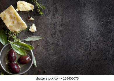 Food background with parmesan cheese, fresh herbs and olives, over dark slate.  Lots of copy space.